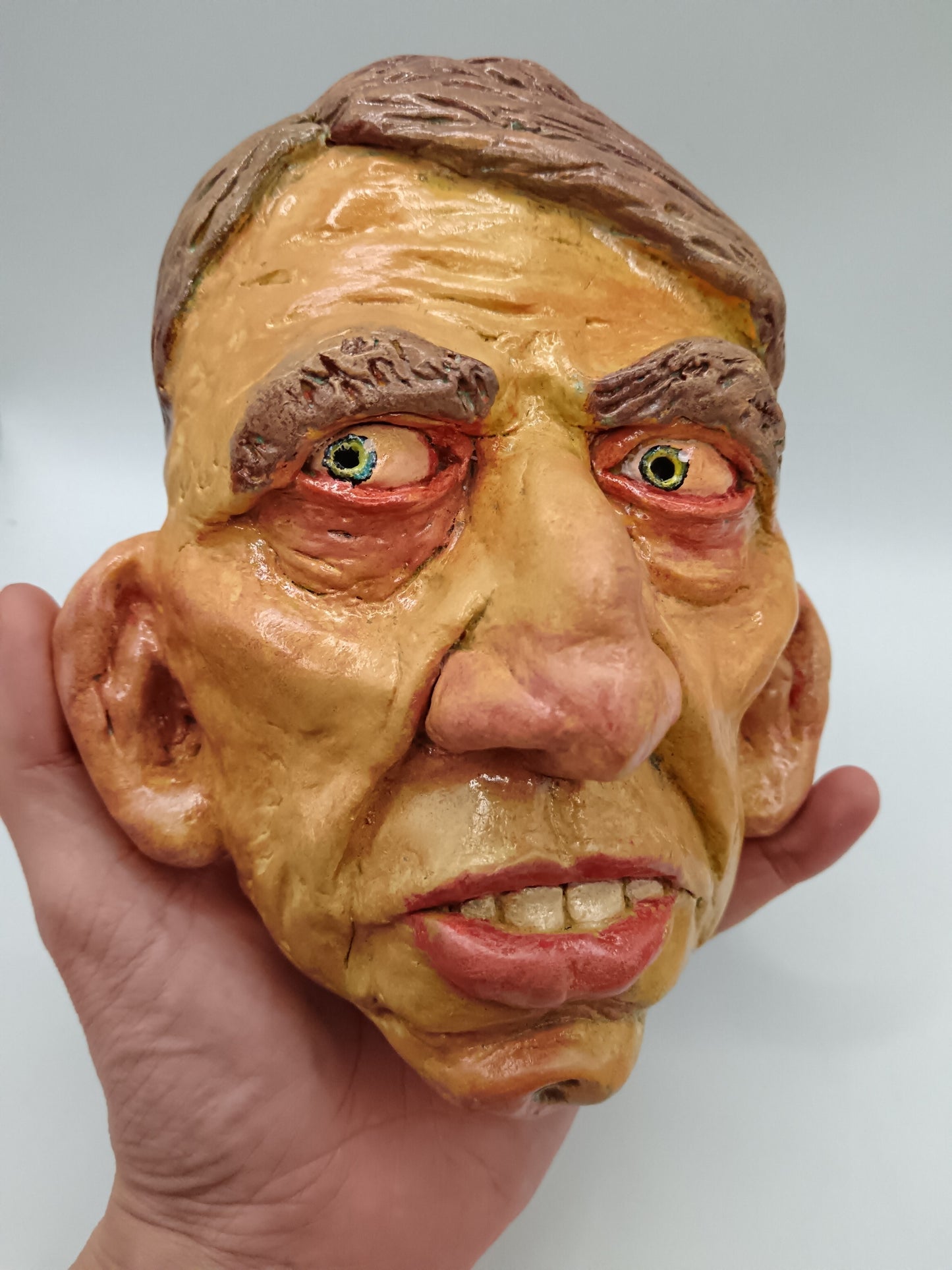 Hand holding a textured mask resembling a human face against a plain background