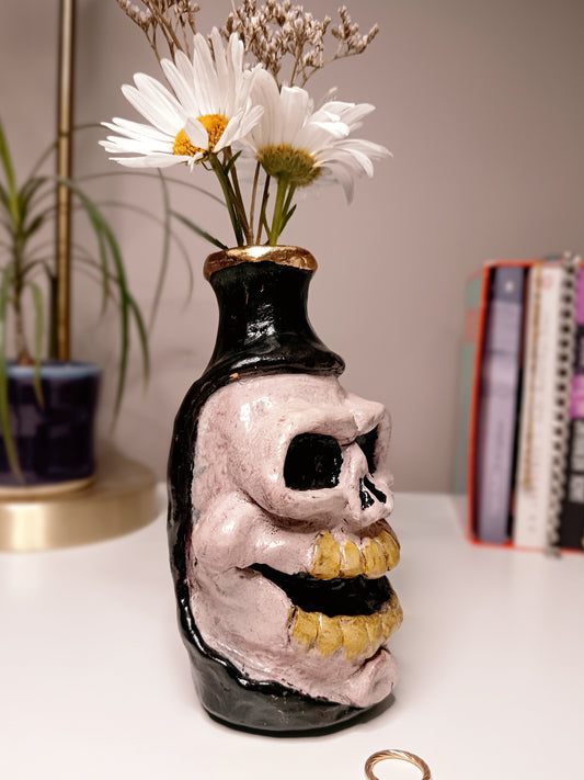 Skull-shaped vase with flowers on a surface side view