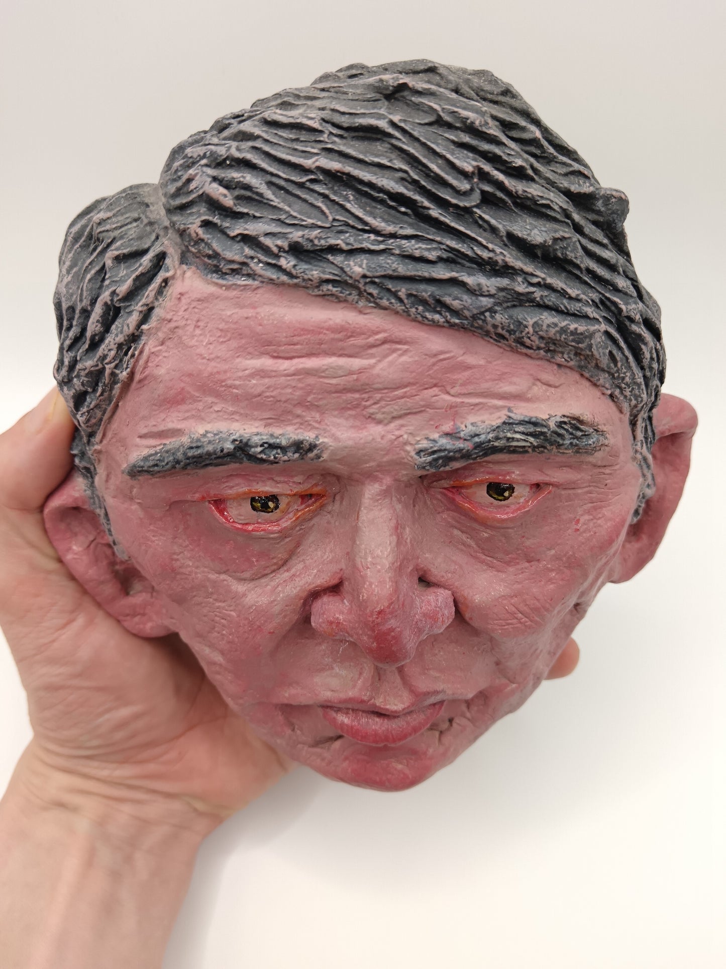 Close-up of a textured head sculpture held by a hand against a white background