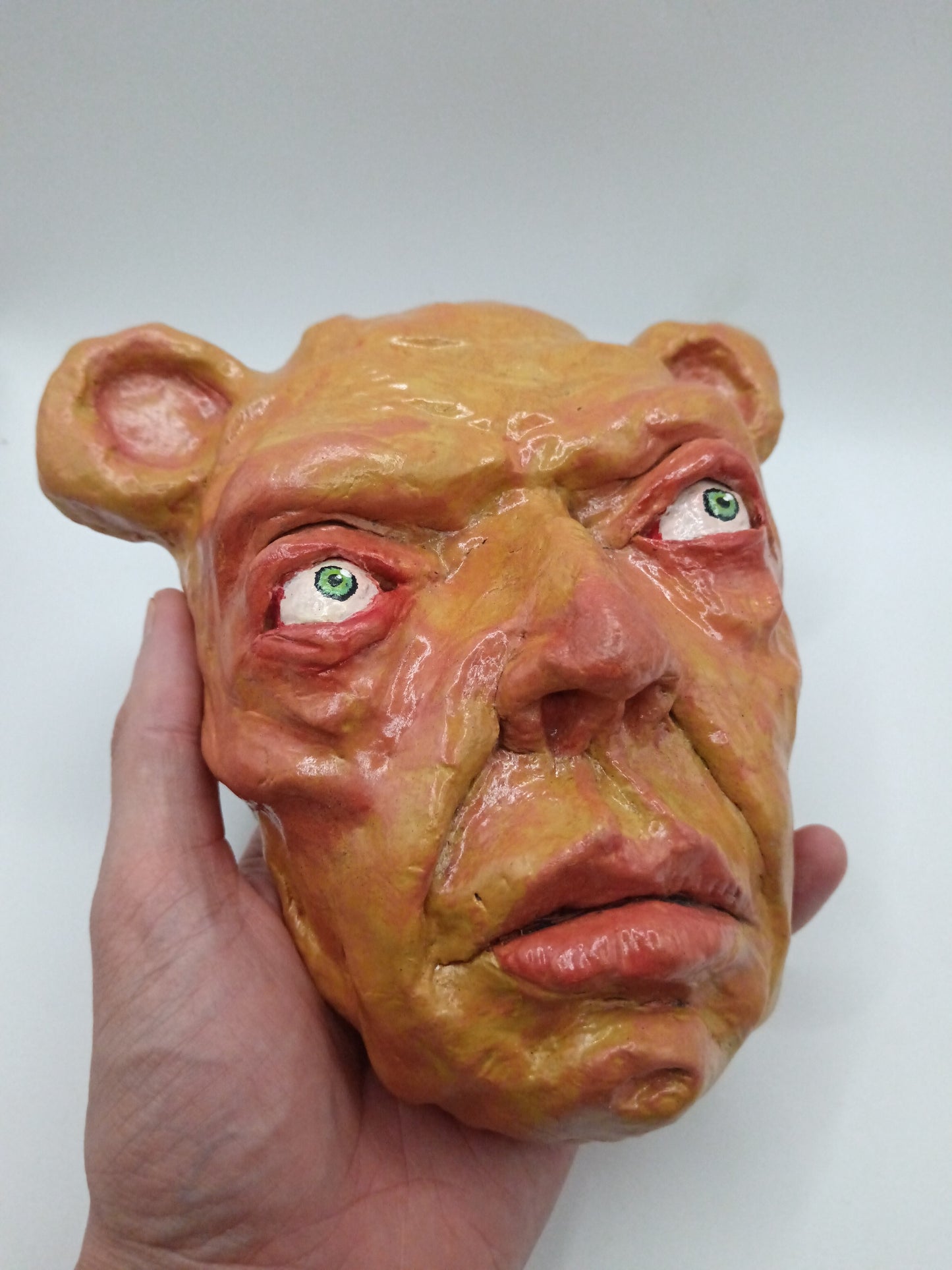 Hand holding a mask with a distorted face on a white background