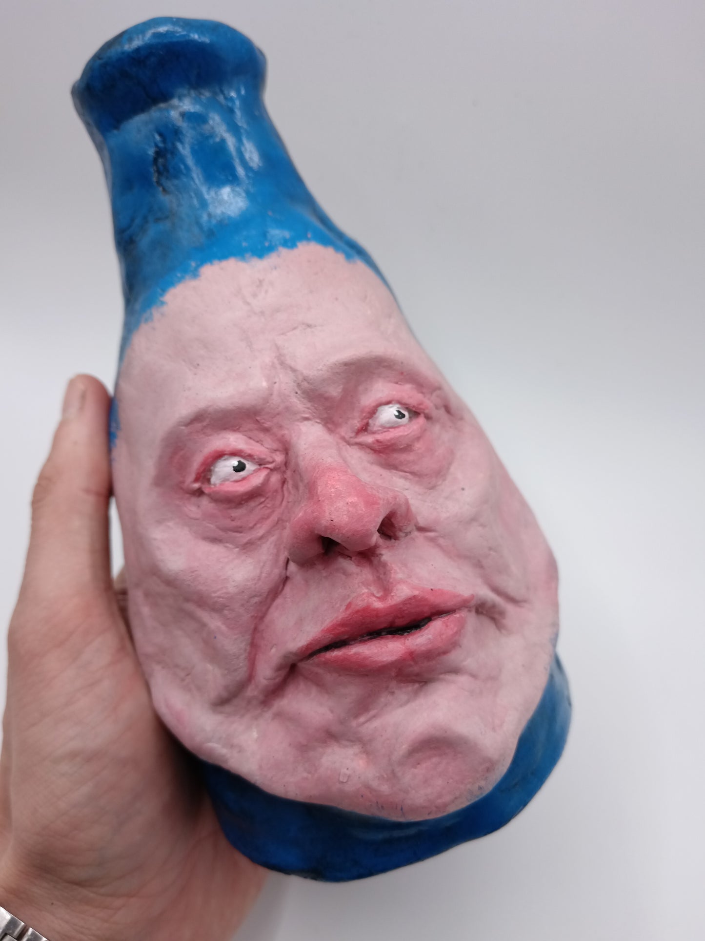 Artistic representation of a face with blue top and pink bottom held by a hand against a white background