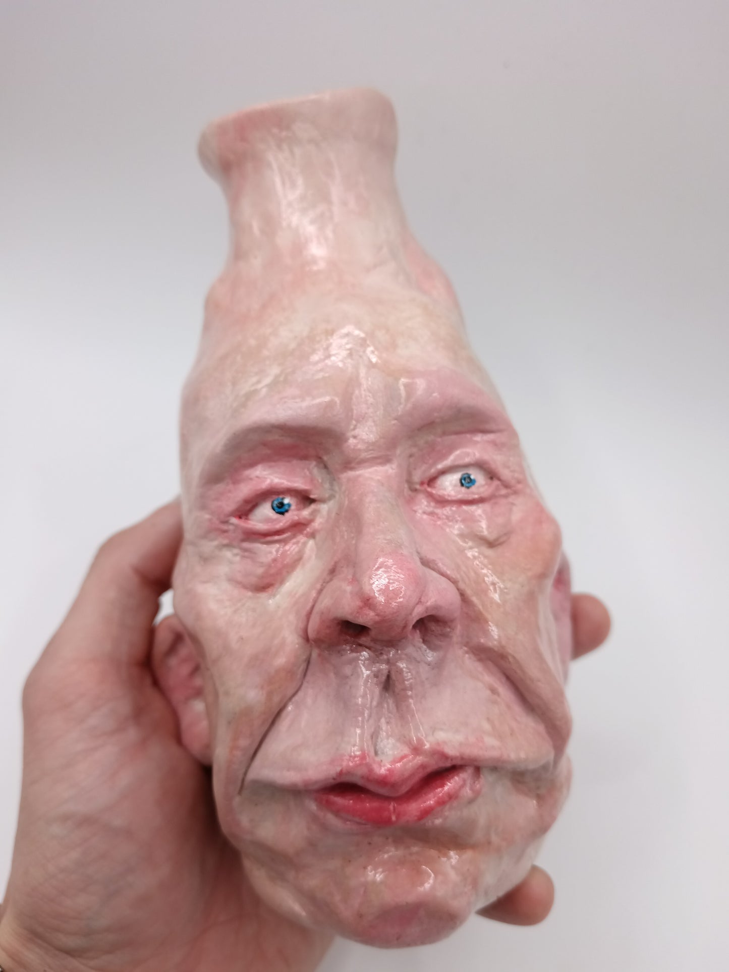 Vase shaped like a human face with a hand holding it against a white background