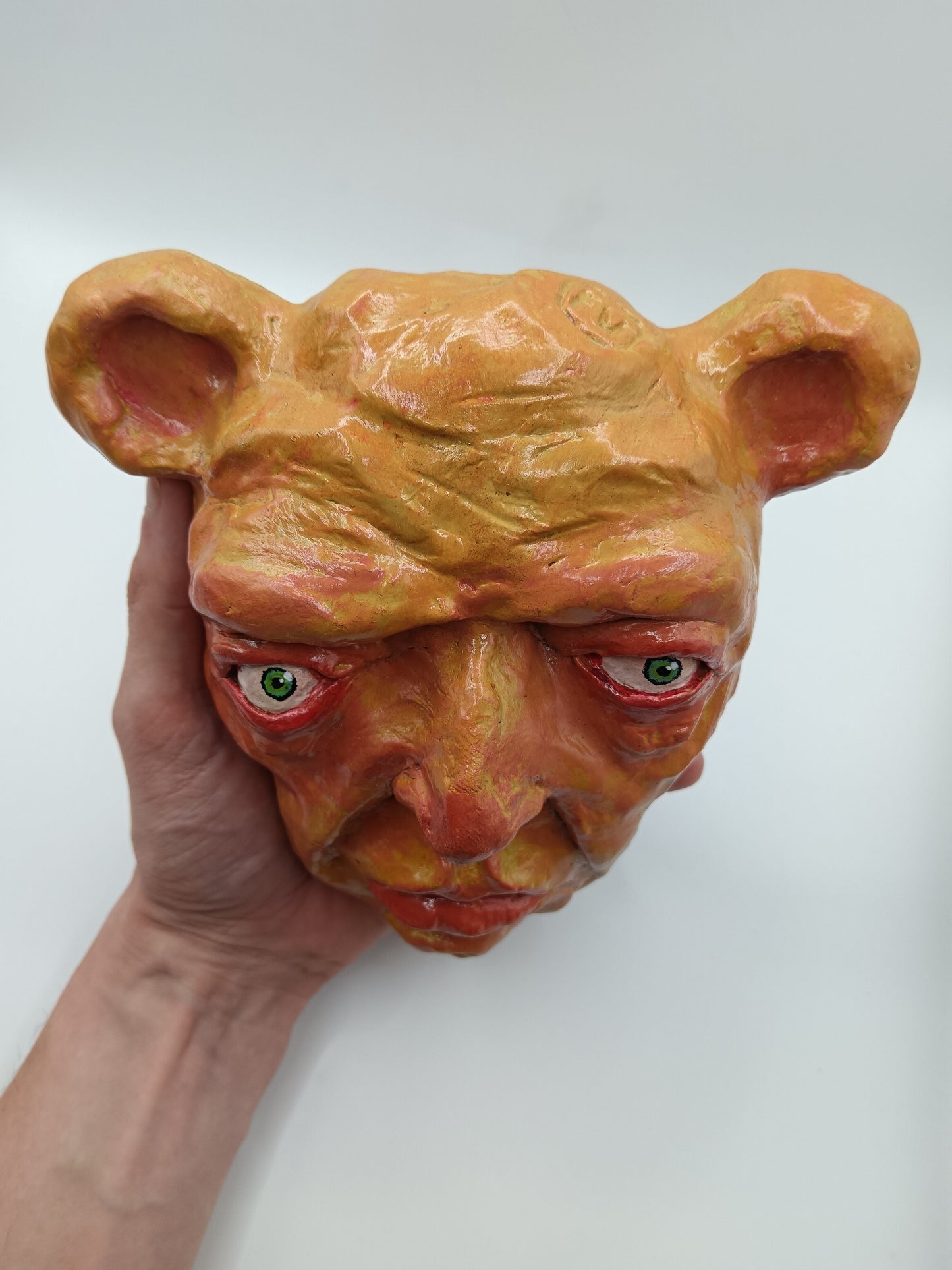 Hand holding a mask with a bear-like design on a white background