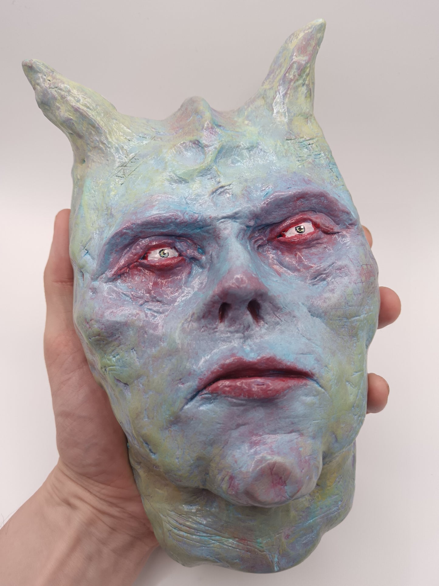 Hand holding a mask with demonic features against a plain background