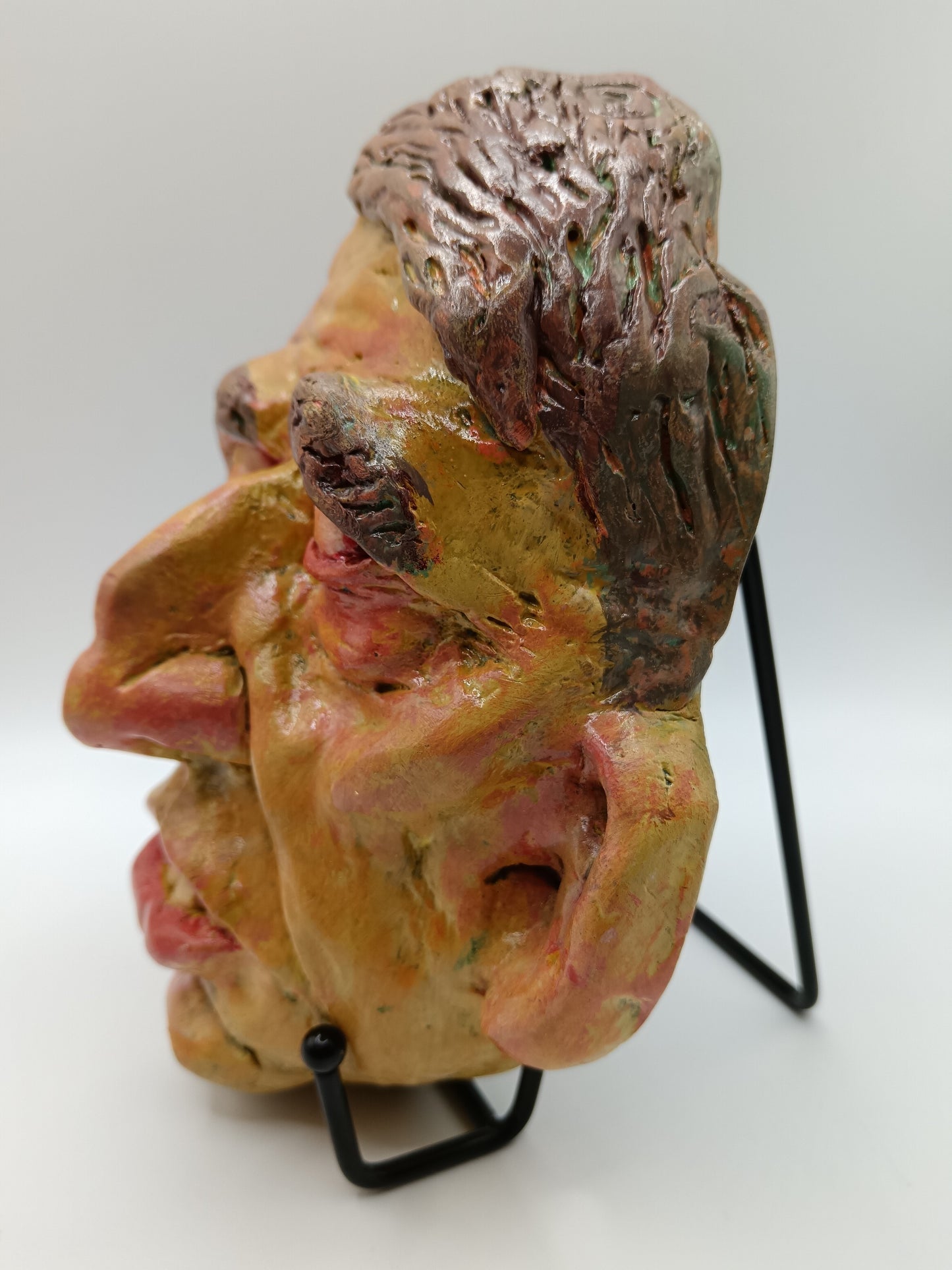 Hand sculpted clay yellow face mask sculpture with stand side view