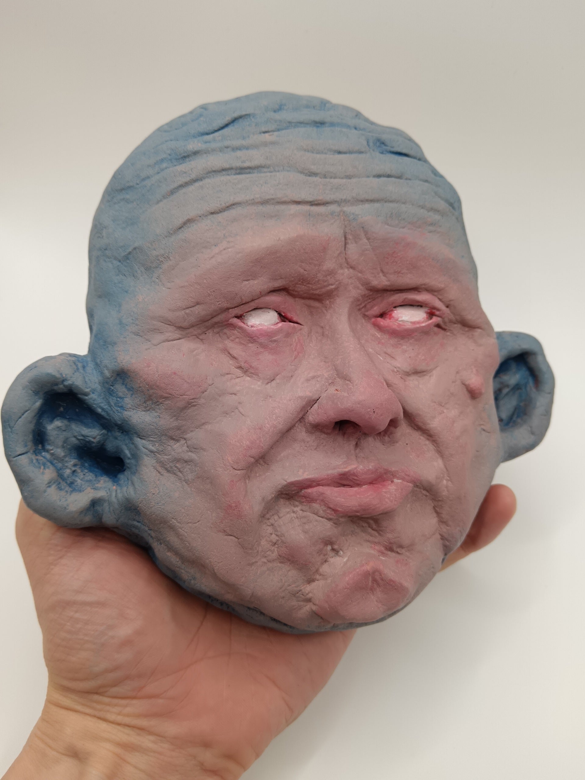 Hand holding a textured, gray mask with large ears against a plain background