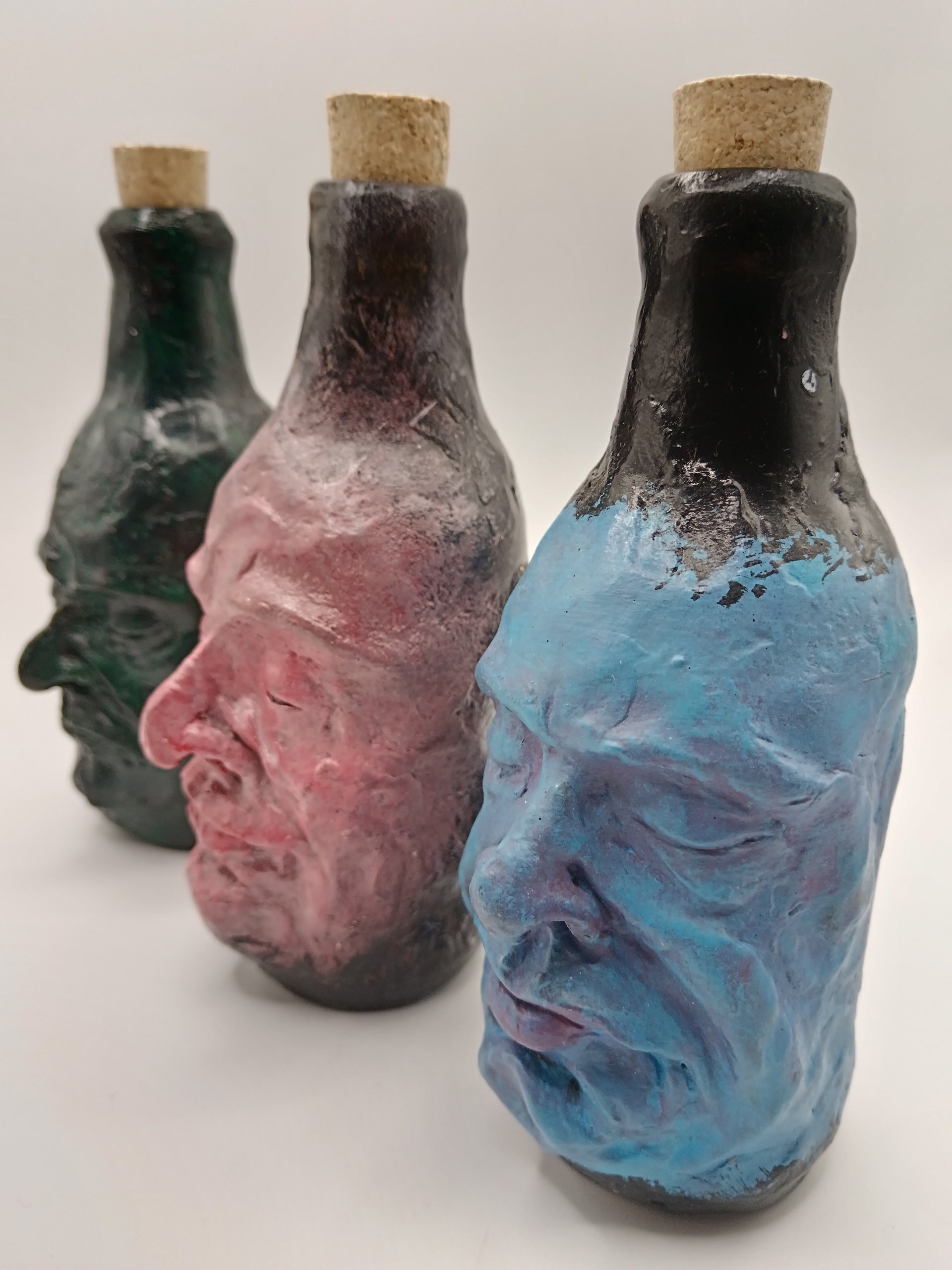 Three bottles shaped like faces with cork stoppers on a white background