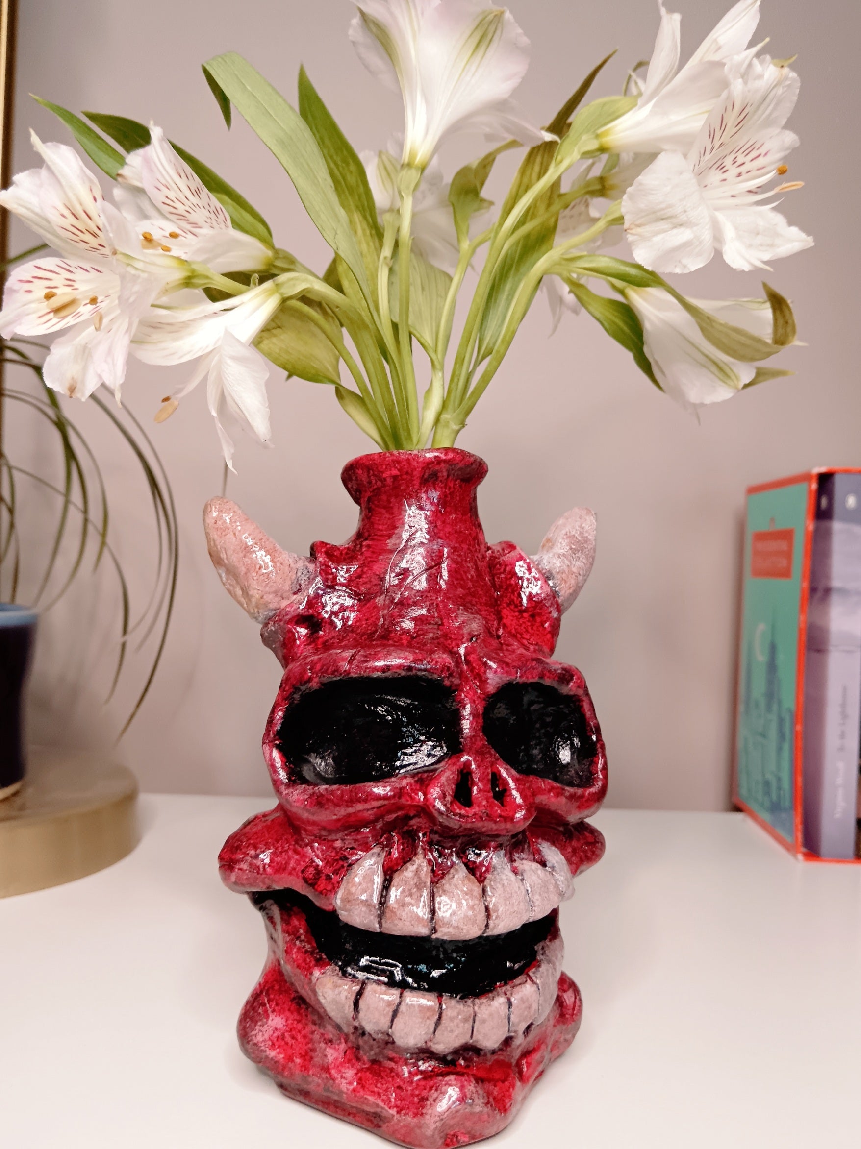 Red skull-shaped vase with white flowers on a white surface