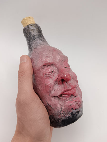 Bottle shaped like a face held by a hand against a white background
