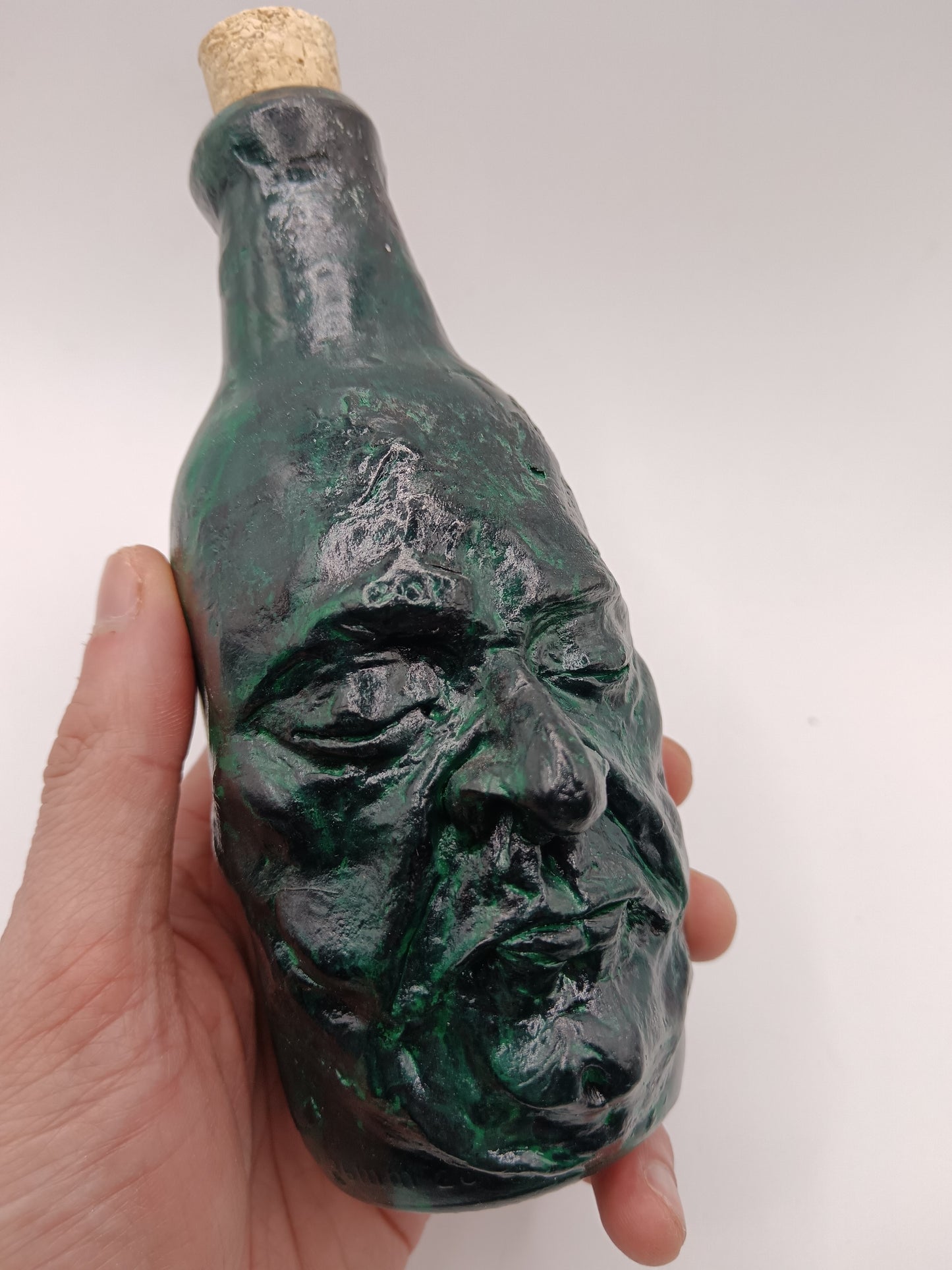 Green bottle shaped like a face held by a hand against a white background