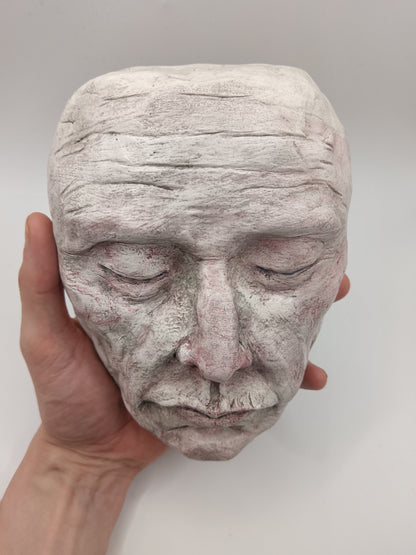 Hand holding a textured ceramic face sculpture against a plain background