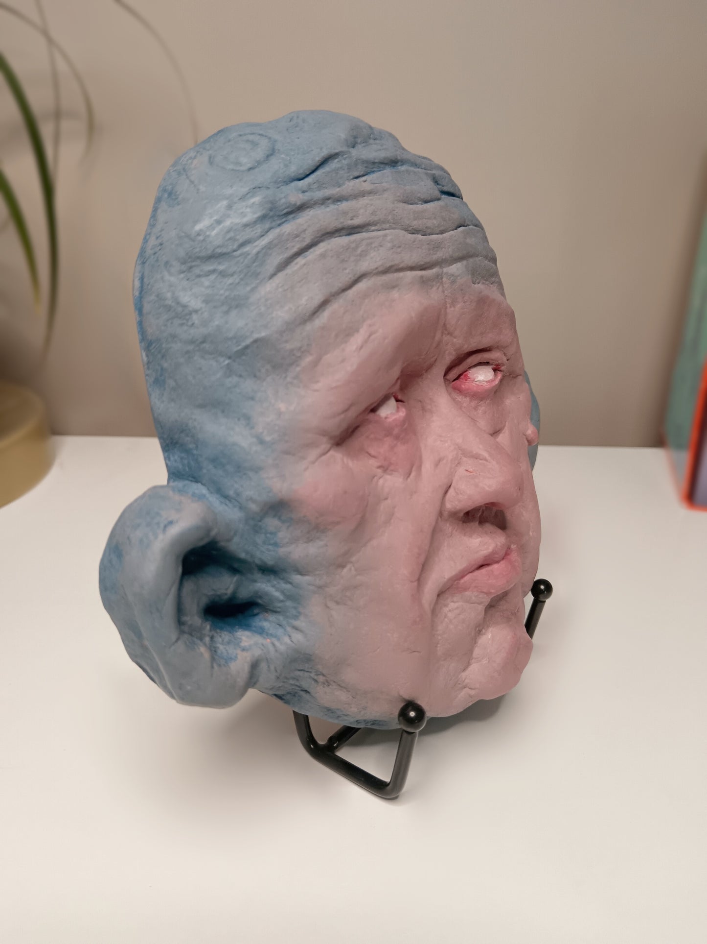 Blue face Handmade sculpture on stand, home setting side view
