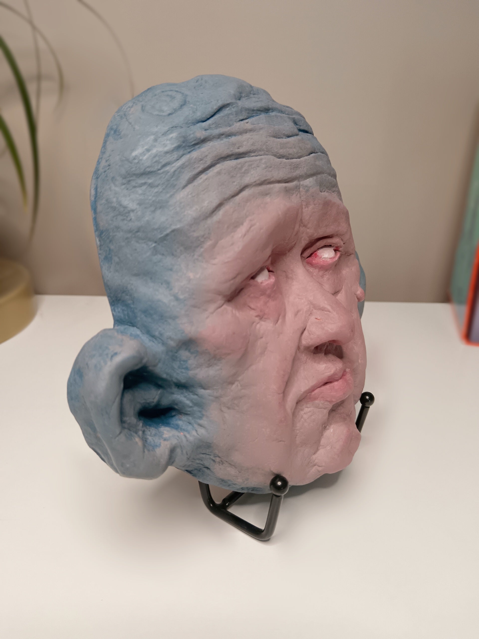 Blue face Handmade sculpture on stand, home setting side view
