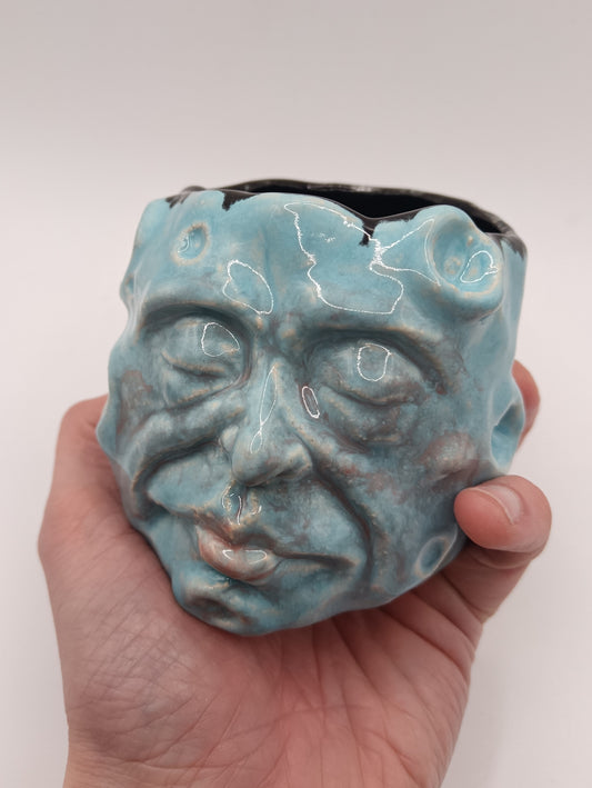 Hand holding a blue ceramic face-shaped planter against a white background