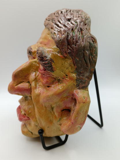 Hand sculpted clay yellow face mask sculpture with stand side view